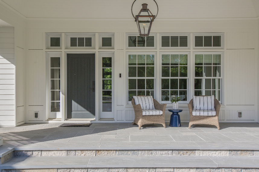 dark grey front door with white trim and siding and a stone patio